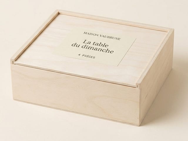 Coffret de bois clair fermé, vu de trois quarts sur un fond de papier écru ; l’étiquette collée sur le couvercle porte le nom du coffret et le nombre de pièces.